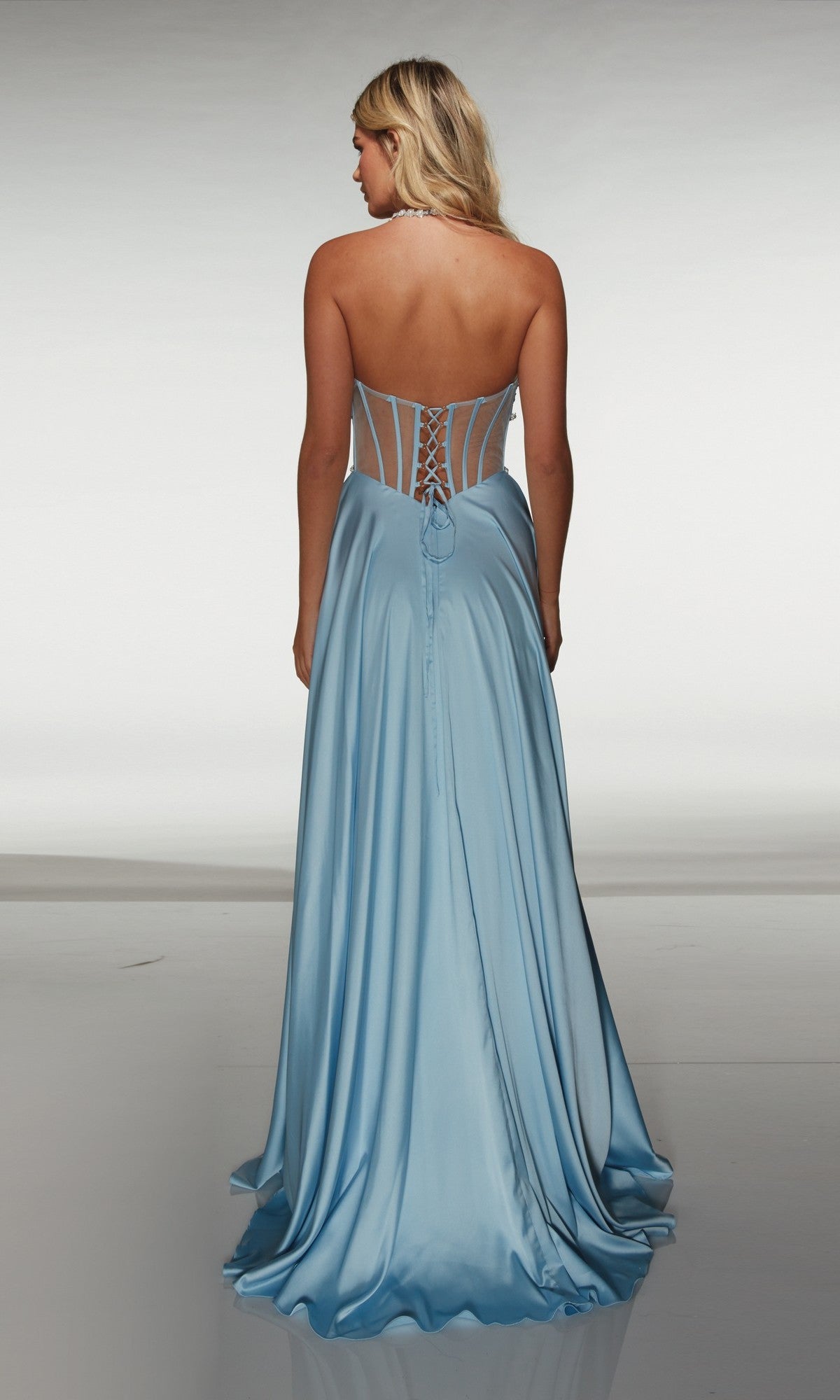 A woman in the Alyce 62064 long prom dress, a light blue strapless gown with a lace-up corset back and classic A-line silhouette, stands facing away against a plain background.